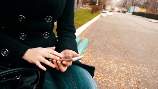 Junge-Frau-mit-Smartphone-auf-einer-Bank-im-Stadtpark