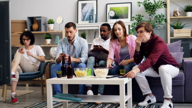 Männer-und-Frauen,-die-Smartphones-benutzen,-schauen-sich-dann-gemeinsam-zu-Hause-Nachrichten-im-Fernsehen-an