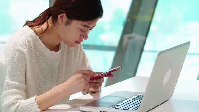 pretty-young-asian-woman-using-mobile-phone-and-laptop-indoor