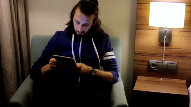 Hübsche,-junge-Mann-mit-Tablet-Computer-auf-Stuhl-zu-Hause-sitzen