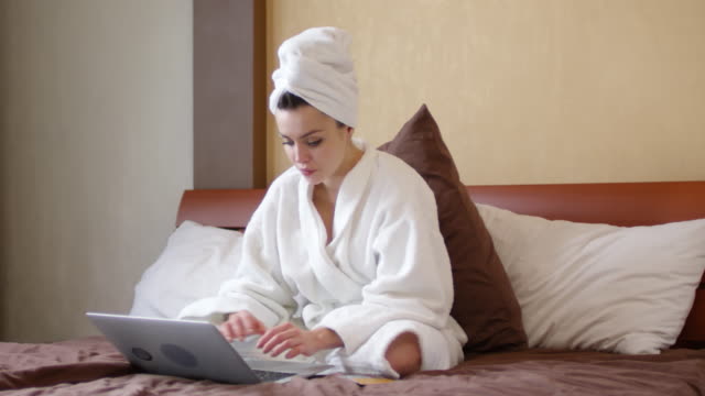 Frau-mit-Handtuch-am-Kopf-mit-Laptop-auf-Bett