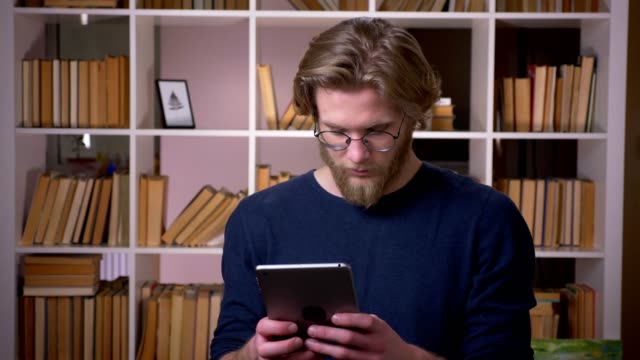 Closeup-shoot-of-adult-attractive-male-student-using-the-tablet-in-the-university-library-indoors
