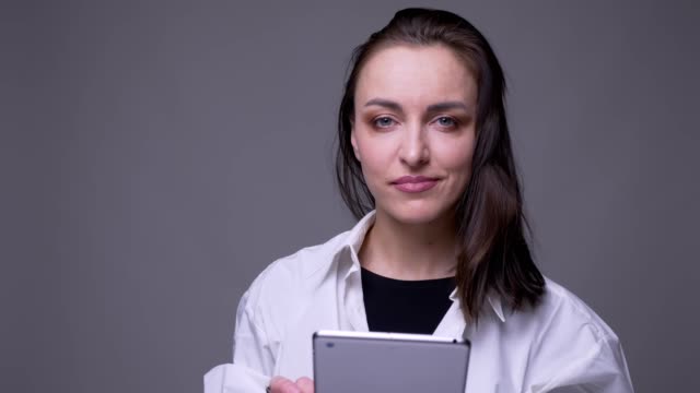 Nahaufnahme-Porträt-von-erwachsenen-attraktiven-kaukasischen-Frau-mit-dem-Tablet-und-lächelnd-Blick-auf-die-Kamera-mit-Hintergrund-isoliert-auf-grau