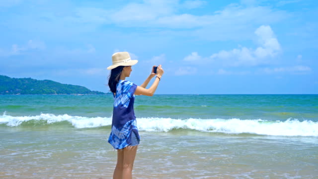 Glückliche-asiatische-Frau-mit-Handy,-um-ein-Foto-mit-der-Kamera-auf-Social-Media-am-Strand-während-Der-Reise-Urlaub-Urlaub-im-Freien-am-Meer-oder-Natur-Meer-am-Mittag,-Phuket,-Thailand