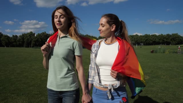Happy-girlfriends-with-lgbt-flag-walking-on-lawn