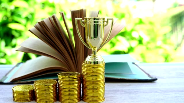 Saving-moneys-for-education-graduate-in-achievement-success-concept:-Rising-coins-with-golden-trophy-winner,stack-books,graduation-hat.-Management-study-competition-leadership-inspiration-in-life
