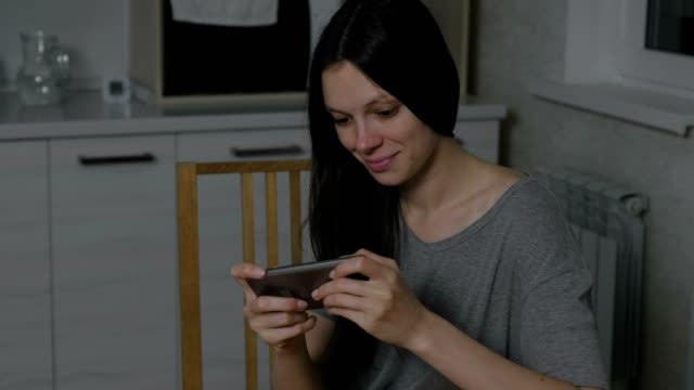 Beautiful-young-woman-stealthily-playing-games-on-mobile-phone-in-the-kitchen-at-night.