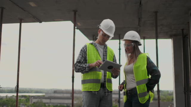 Bauarbeiter-Mann-und-Architekt-Frau-in-einem-Helm,-diskutieren-den-Plan-des-Baus-des-Hauses,-erzählen-einander-über-den-Entwurf,-halten-eine-Tablette,-Blick-auf-die-Zeichnungen,-Hintergrund-der-Sonnenstrahlen