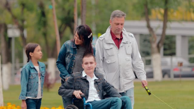 El-joven-con-discapacidad-está-en-la-ciudad-con-su-familia.-Mamá-cariñosa-lleva-a-su-hijo-en-silla-de-ruedas.