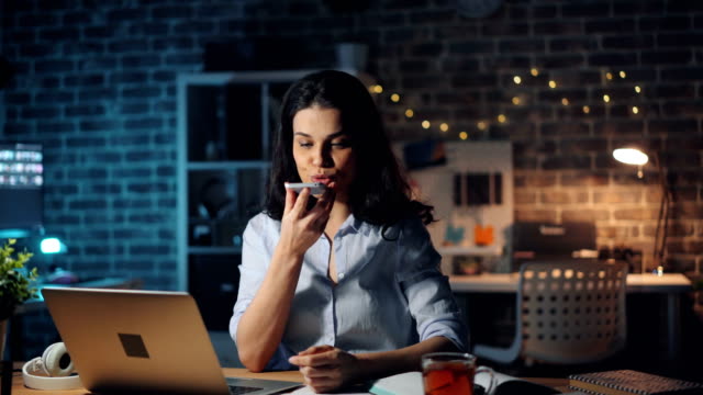 Young-lady-using-smartphone-touching-screen-talking-working-overtime-at-night