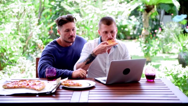 Gay-couple-having-pizza-for-lunch.-Biting-pizza,-talking.