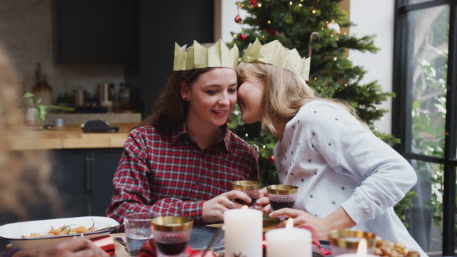 Pareja-gay-mujer-sentada-alrededor-de-la-mesa-para-la-cena-de-Navidad-susurrando-y-haciendo-tostadas