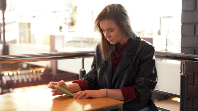 Young-beautiful-caucasian-girl-sitting-in-a-cafe-looking-at-the-phone-screen-gets-bad-news-and-is-upset.
