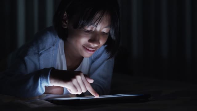Asiática-niña-toca-la-pantalla-en-la-tableta-digital-moderna-en-el-dormitorio-por-la-noche.