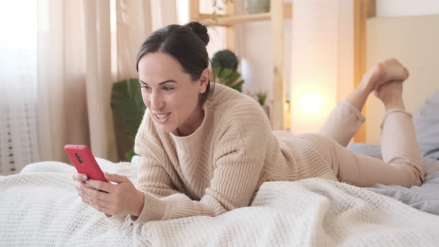 Woman-using-mobile-phone-and-singing-song-while-relaxing-on-bed