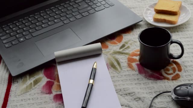 Frühstückskaffee-im-Morgensonnenschein-mit-Laptop-Computer-schwarz-Farbstift-und-weiß-regiert-Papier-Notebook,-Keramik-Tasse-Untertasse-und-Keks-auf-Top-Büro-Platz-Schreibtisch-Hintergrund.-Lifestyle-Image.
