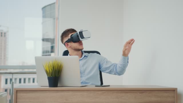 Ein-junger-Mann,-der-an-einem-Schreibtisch-im-Büro-sitzt,-verwendet-Augmented-Reality-Brillen,-um-an-Geschäftsprojekten-in-verschiedenen-Bereichen-zu-arbeiten.