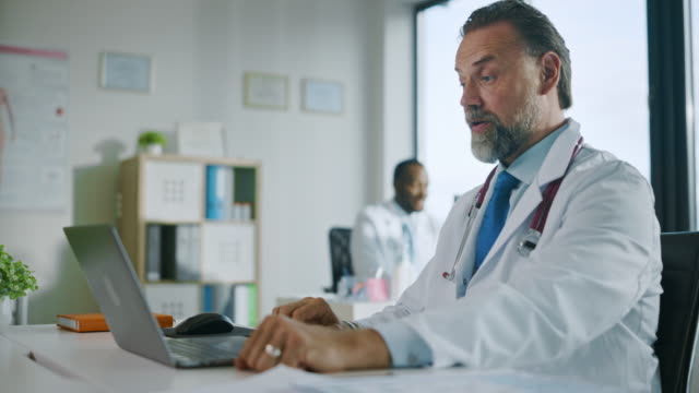 Hausarzt-macht-einen-Videoanruf-mit-Patient-auf-Laptop-Computer-in-einer-Gesundheitsklinik.-Physician-in-Lab-Coat-spricht-über-Gesundheitsprobleme-und-Diagnose-im-Krankenhausbüro.