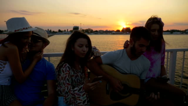Gruppe-von-Freunden-auf-einer-Bank-sitzen-und-singen-auf-einer-Brücke-über-das-Meer-in-Zeitlupe