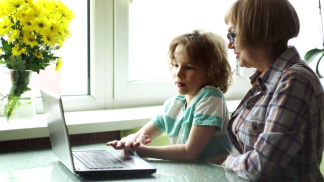 Der-Junge-jüngeren-Schulalter-hilft-der-älteren-Frau,-den-Computer-zu-beherrschen.