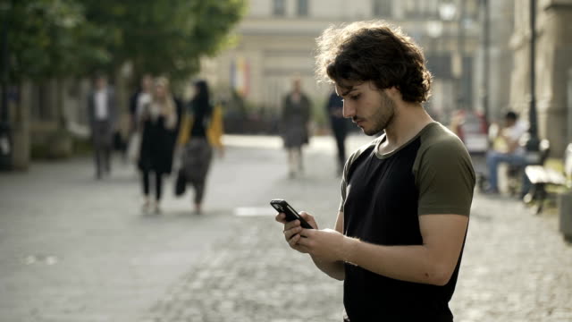 Guapo,-esperando-en-un-lugar-urbano-público-para-mensajes-de-texto-de-amigos-en-los-medios-de-comunicación-social-de-la-aplicación-en-su-smartphone