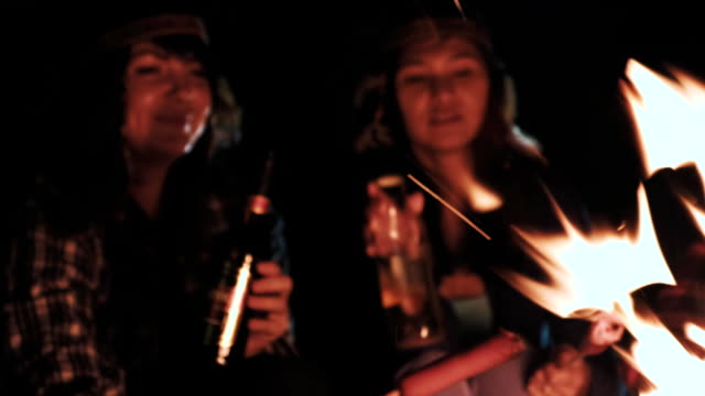 junges-Paar-Getränk-trinken-und-dabei-anstoßen-in-der-Nähe-von-Feuer-im-nächtlichen-Wald,-Liebhaber-trinken-Alkohol-und-macht-Toasten-im-freien-Glas,-Mann-mit-Mädchen-jubelt-Bier-in-Reisen-Camp-im-Wald