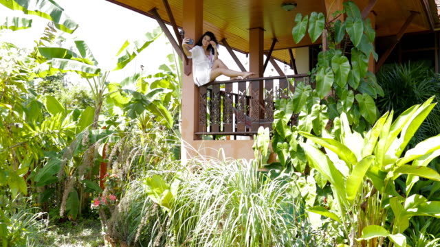 Junge-Frau-fotografieren-Selfie-auf-Smart-Handy-sitzen-auf-Balkon-In-Villa-In-tropischem-Wald,-schöne-Mädchen,-das-Selbstporträt