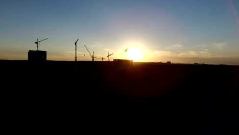 Aerial-shot-of-crans,-building-and-forest-at-sunset.