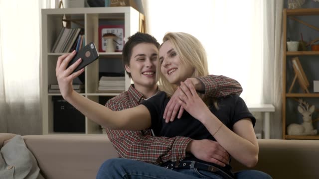 Zwei-junge,-schöne-Mädchen-sitzen-auf-der-Couch-und-Herstellung-von-Selfies,-Lesben,-LGBT-60-fps