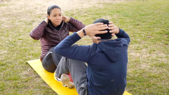 Paar-Training-im-Freien.-Lateinamerikanische-junges-Paar-setzen-Sie-Ups-auf-gemeinsamen-gelbe-Matte-im-Herbst-regnerischen-Park-als-Teil-der-routinemäßigen-Trainingsprogramm-zusammen.