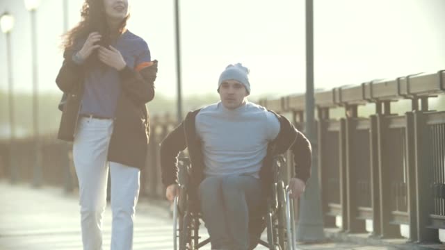 Junge-Behinderte-Mann-im-Rollstuhl-zu-Fuß-mit-junge-Frau-auf-dem-Kai-und-reden
