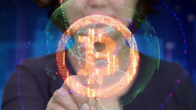 Young-Asian-female-touches-futuristic-holographic-interface-and-activates-Bitcoin-currency-sign