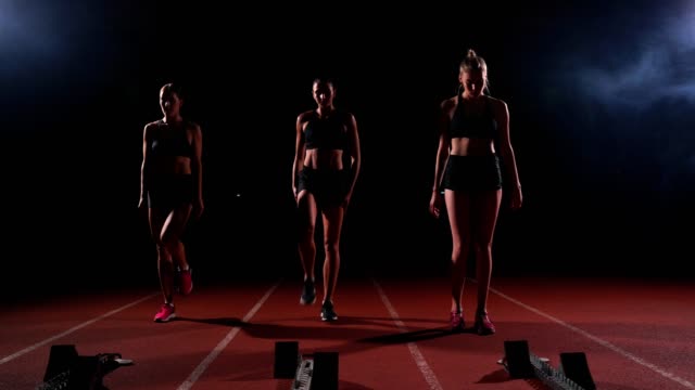 Female-runners-at-athletics-track-crouching-at-the-starting-blocks-before-a-race.-In-slow-motion