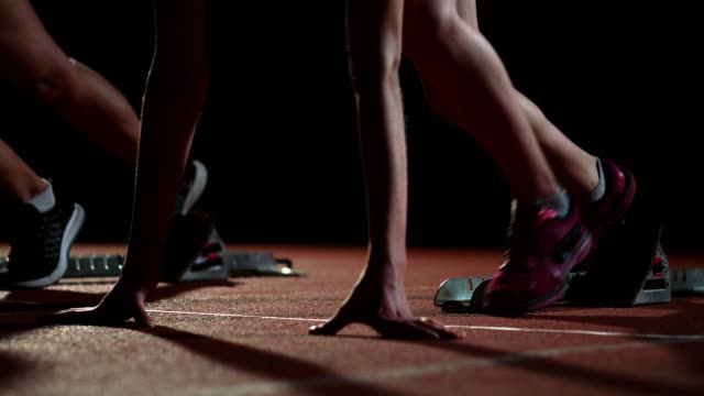 Corredores-femeninos-en-atletismo-pista-agachado-en-los-bloques-de-salida-antes-de-una-carrera.-En-cámara-lenta