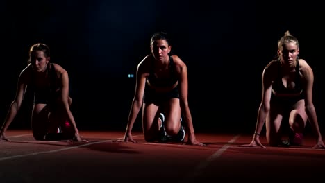 Tres-deportes-a-los-atletas-de-la-chica-por-la-noche-en-el-comienzo-de-la-cinta-de-correr-para-la-carrera-en-la-distancia-sprint-desde-la-posición-sentada