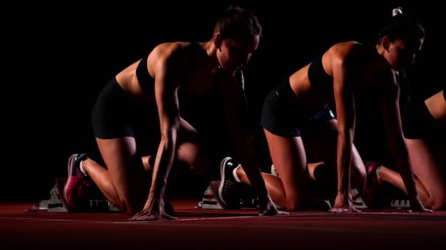 Three-sports-girl-athletes-at-night-on-the-treadmill-start-for-the-race-at-the-sprint-distance-from-the-sitting-position