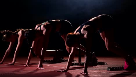 Drei-Mädchen-in-schwarzen-Klamotten-sind-in-der-Start-Pads-zum-start-des-Rennens-am-Wettbewerb-im-Lichte-der-Lichter-und-laufen-in-Richtung-Ziel