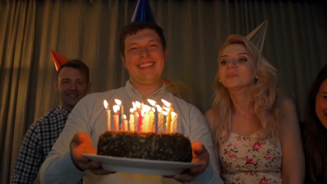 Happy-guy-with-friends-bringing-birthday-cake-to-You