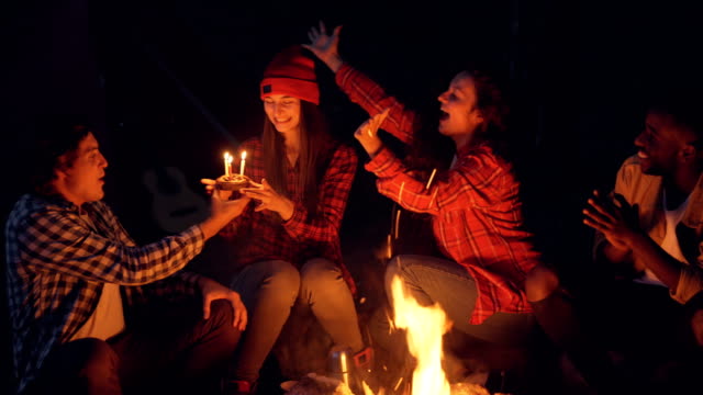 Attraktive-junge-Frau-Wanderer-feiert-Geburtstag-im-Wald-immer-Kuchen-Kerzen-Ausblasen,-während-ihre-Freundinnen-sind-Hände-klatschten-und-schreien.-Feier-und-Natur-Konzept.