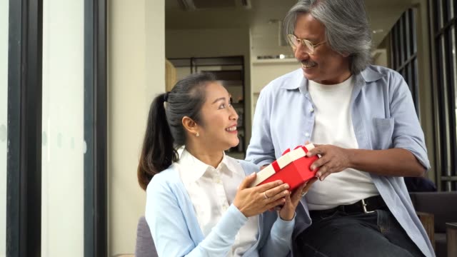 Couple-of-middle-aged-woman-and-senior-man-giving-a-surprise-gift-on-her-special-day-such-as-birthday-or-wedding-anniversary.-Celebration-and-holiday-concept