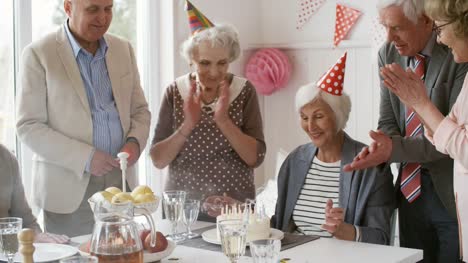 Ältere-Frau-Ausblasen-der-Kerzen-auf-Geburtstagsparty-mit-Freunden