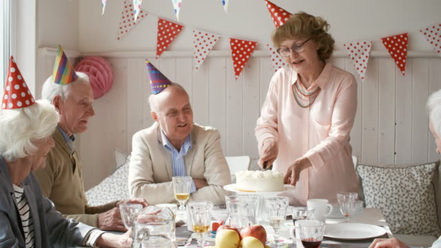 Happy-Senior-Woman-Cutting-Geburtstagskuchen-für-Gäste