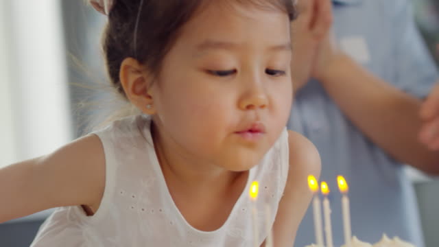 Aufgeregt-asiatische-Mädchen-bläst-Kerzen-auf-Kuchen