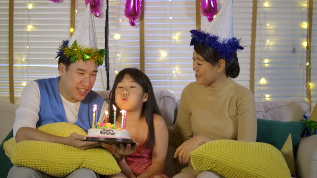 Eine-niedliche-kleine-asiatische-Mädchen-feiern-ihren-Geburtstag-mit-einer-Torte-und-glückliche-Familie.-Sie-gibt-ein-breites-Lächeln-und-ihre-Familie-begrüßen-sie.-In-Zeitlupe.