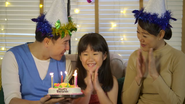 Una-linda-asiática-niña-celebrando-su-cumpleaños-con-un-pastel-y-una-familia-feliz.-Ella-le-da-una-gran-sonrisa-y-su-familia-aplaudirla.-En-cámara-lenta.