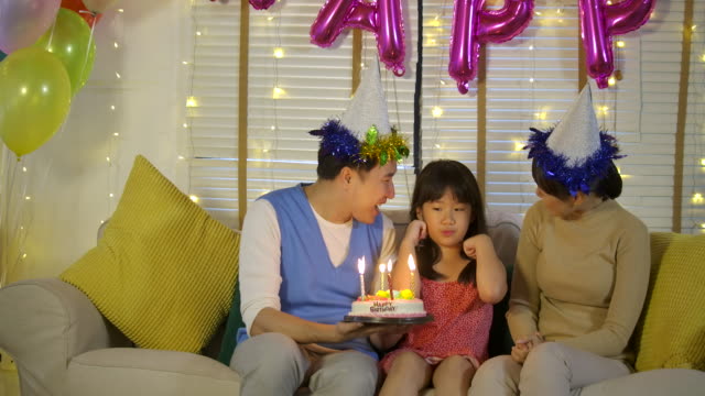 Eine-niedliche-kleine-asiatische-Mädchen-feiern-ihren-Geburtstag-mit-einer-Torte-und-glückliche-Familie.-Sie-gibt-ein-breites-Lächeln-und-ihre-Familie-begrüßen-sie.-In-Zeitlupe.