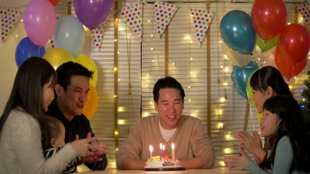 Glücklich-asiatischen-Mann-sitzt-am-Tisch,-umgeben-von-seiner-Familie-und-seinen-Freunden-feiert-seinen-Geburtstag-mit-einer-Torte.