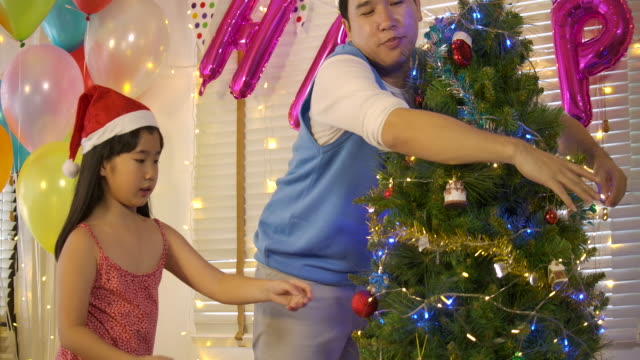Asian-Father-and-daughter-decorating-the-Christmas-tree--in-slow-motion