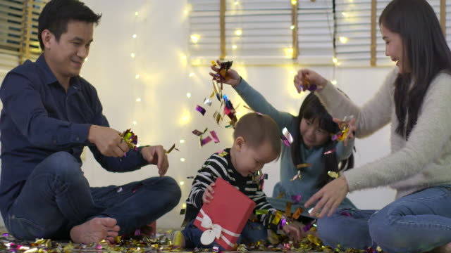 Familia-asiática-feliz-sentado-en-piso-de-sala-de-estar-y-jugar-con-confeti-en-cámara-lenta.