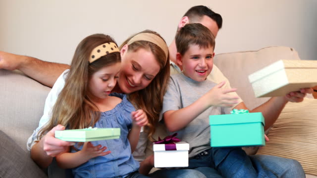 Glückliche-junge-Familie-sitzt-auf-sofa-mit-Geburtstag-präsentiert